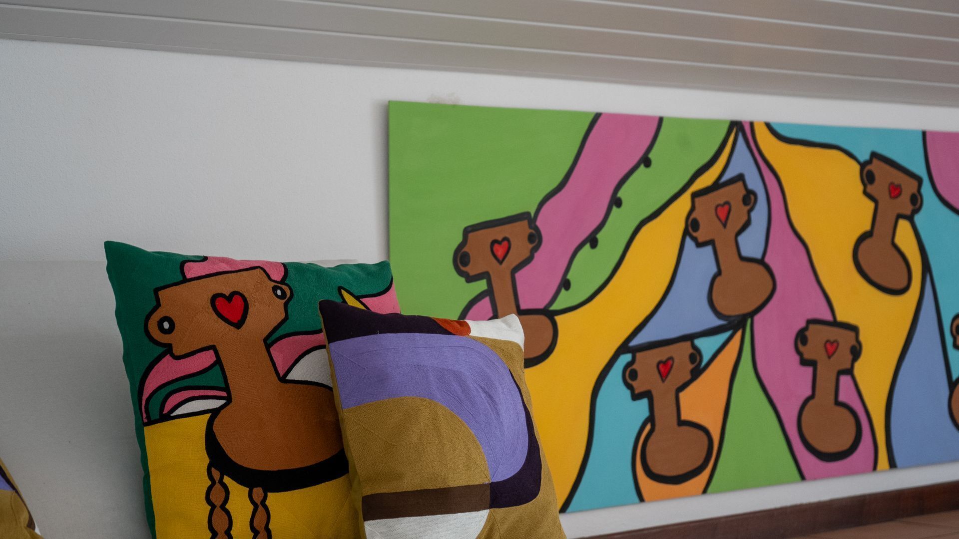 A wall with colorful artwork and two pillows with abstract designs.