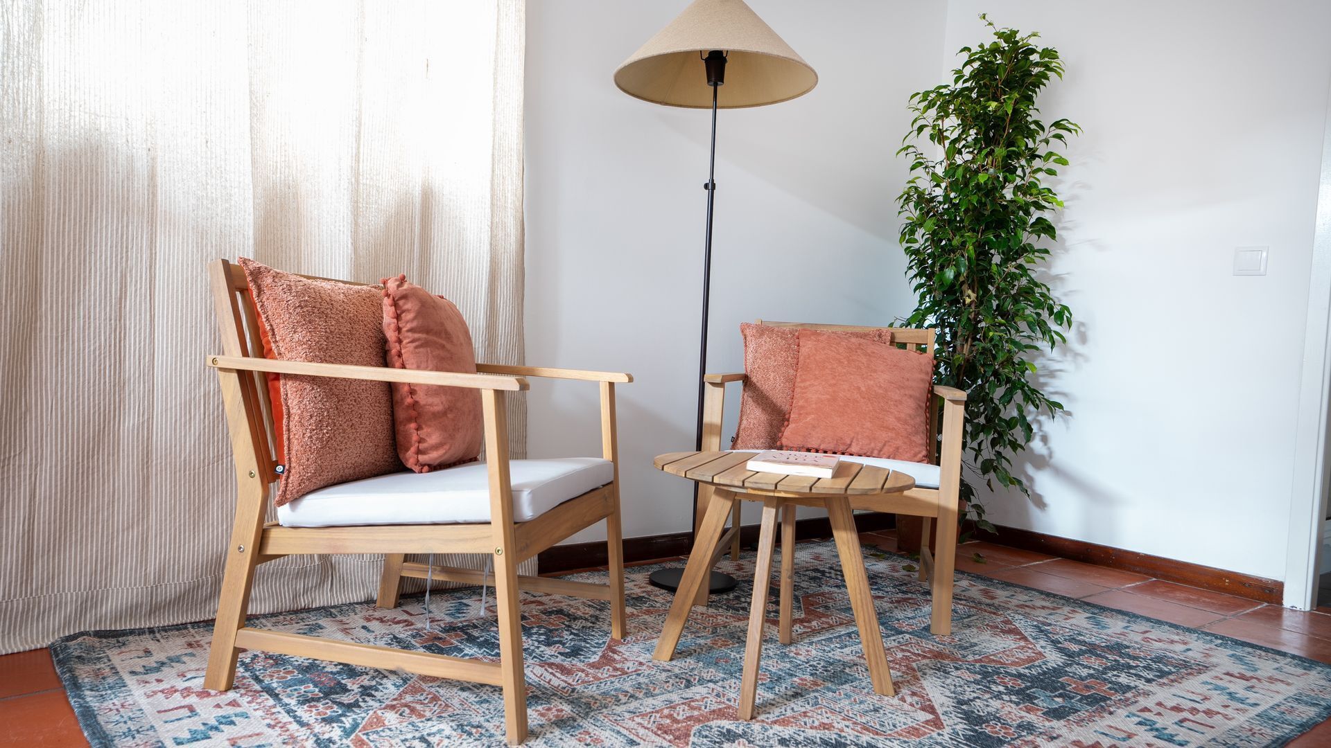 Quarto com duas cadeiras de madeira, uma mesa redonda pequena, um abajur e um vaso com planta.