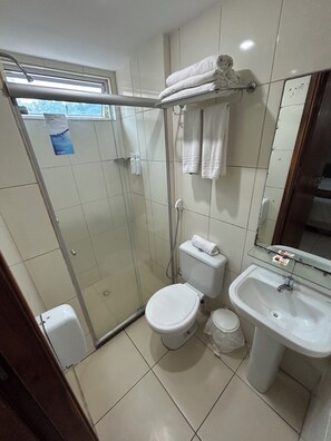 A bathroom with a glass-enclosed shower, a toilet, a sink, and a towel rack with folded towels. - Melhores Flats - Sossego frente ao mar (João Pessoa)