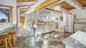Une cuisine spacieuse dotée d’un îlot central, de poutres en bois et d’un sol carrelé.