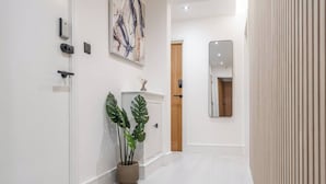 A hallway with a white door, a potted plant, a wooden cabinet, and a mirror on the wall. - Near Anfield | SofaBed & Mini Fridge | Parking (Liverpool)