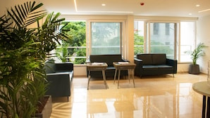 A modern waiting area with a sofa, chairs, and a small table. Large windows offer a view of greenery outside. - Cozy studio in marvelous Pune with AC, WiFi, Yashvantgad. (Pune)