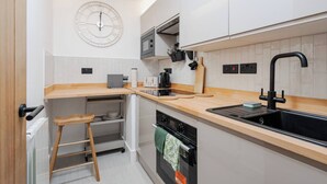 A modern kitchen with white cabinets, a wooden countertop, a black faucet, and a clock on the wall. - Independent | Kitchen, Desk & Washer | Free Parking (Liverpool)