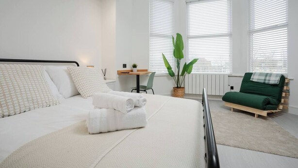 A modern bedroom with a large bed, a desk, a chair, a green sofa, and a potted plant. - Independent | Kitchen, Desk & Washer | Free Parking (Liverpool)