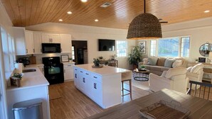 Una cocina moderna con armarios blancos, una isla central y una zona de comedor con mesa de madera.
