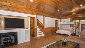 Interior acogedor de una cabaña con chimenea, televisor, litera y escalera.