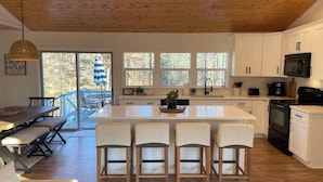 Una cocina moderna con armarios blancos, una isla central con taburetes altos y un amplio ventanal con vistas al exterior.