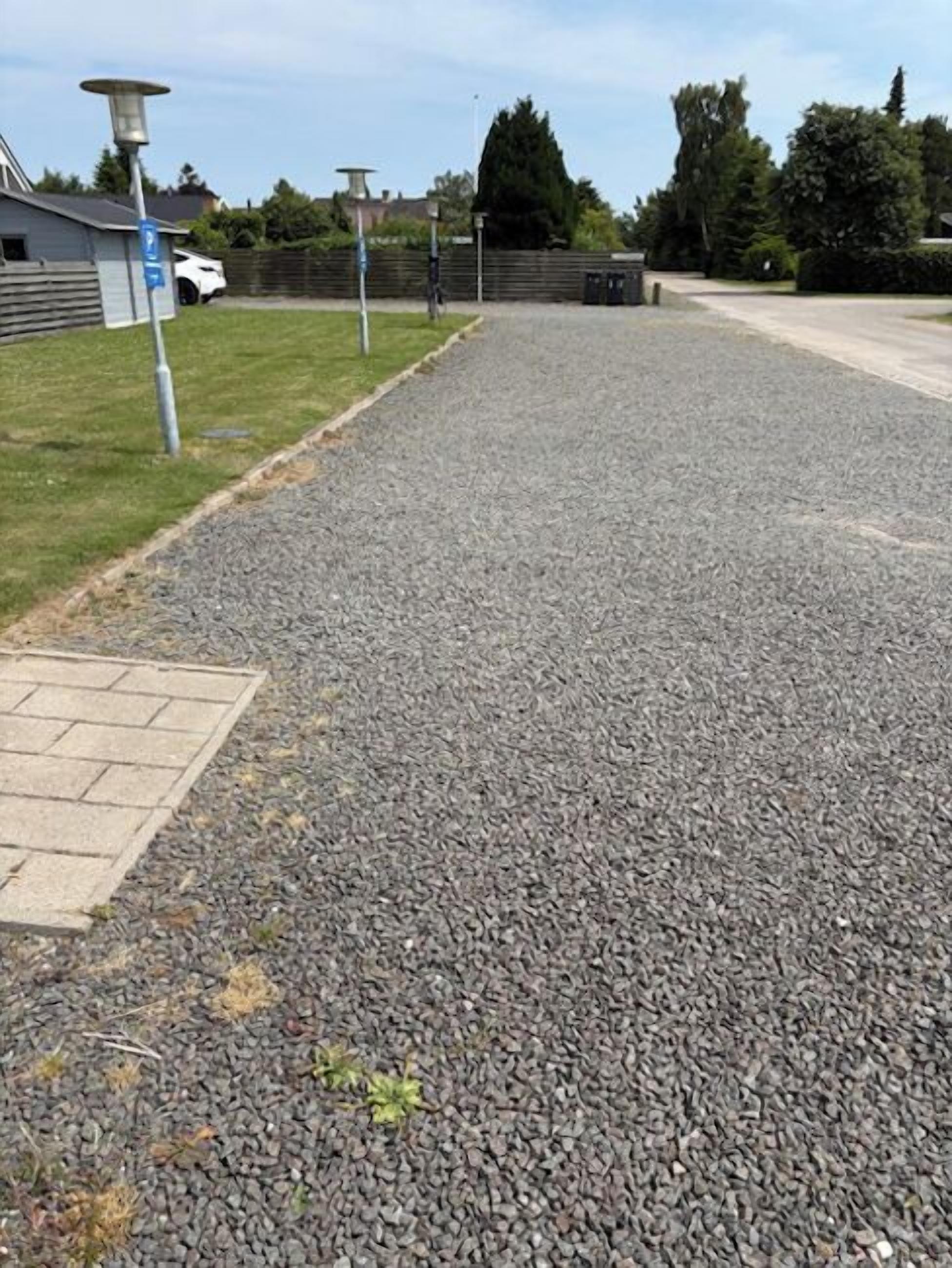 A gravel driveway leading to a building with a blue parking sign.