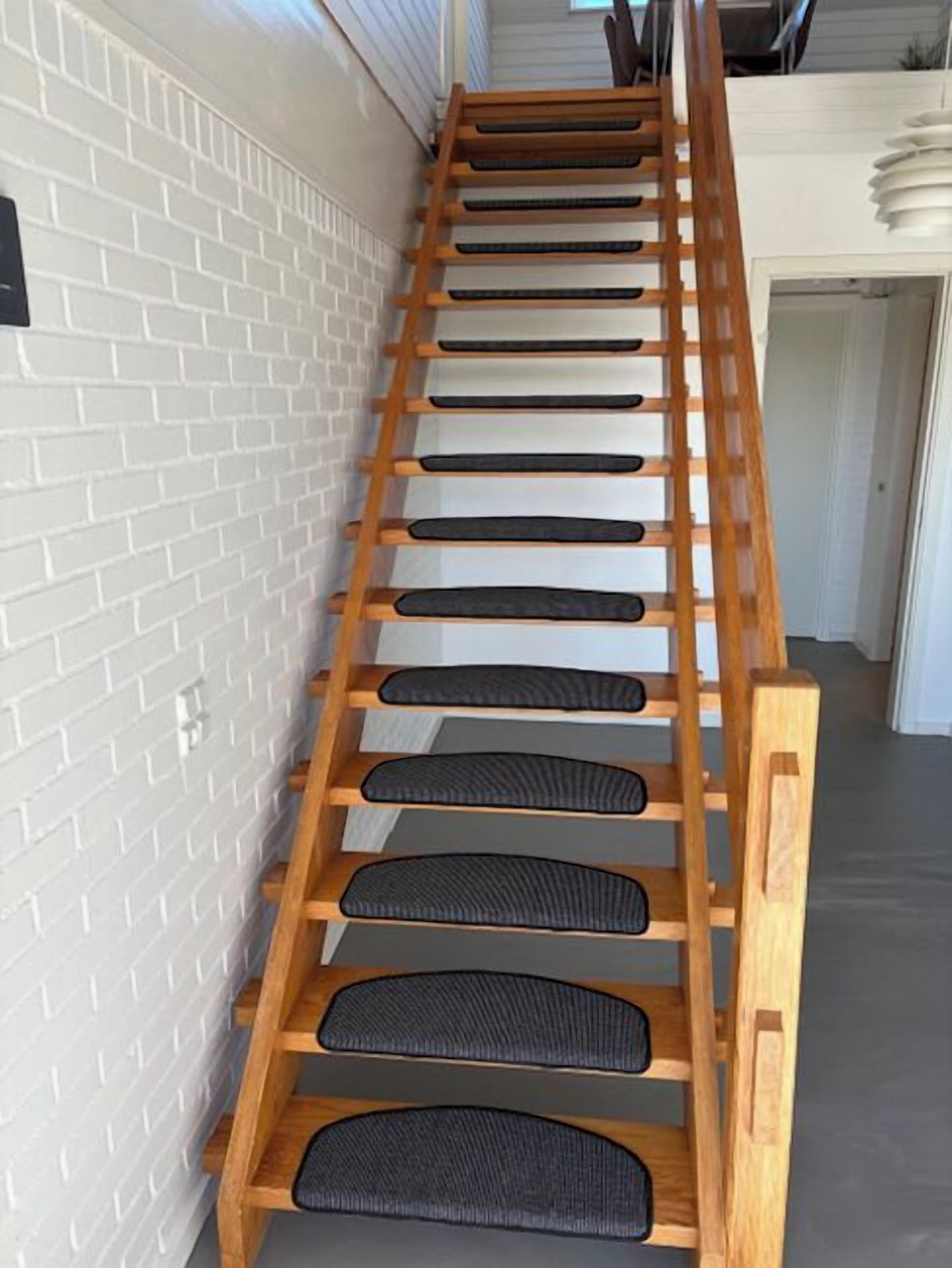 A wooden ladder with black rubber steps against a white brick wall.
