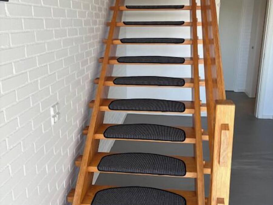 Una escalera de madera con peldaños de caucho negro frente a un muro de ladrillo blanco.