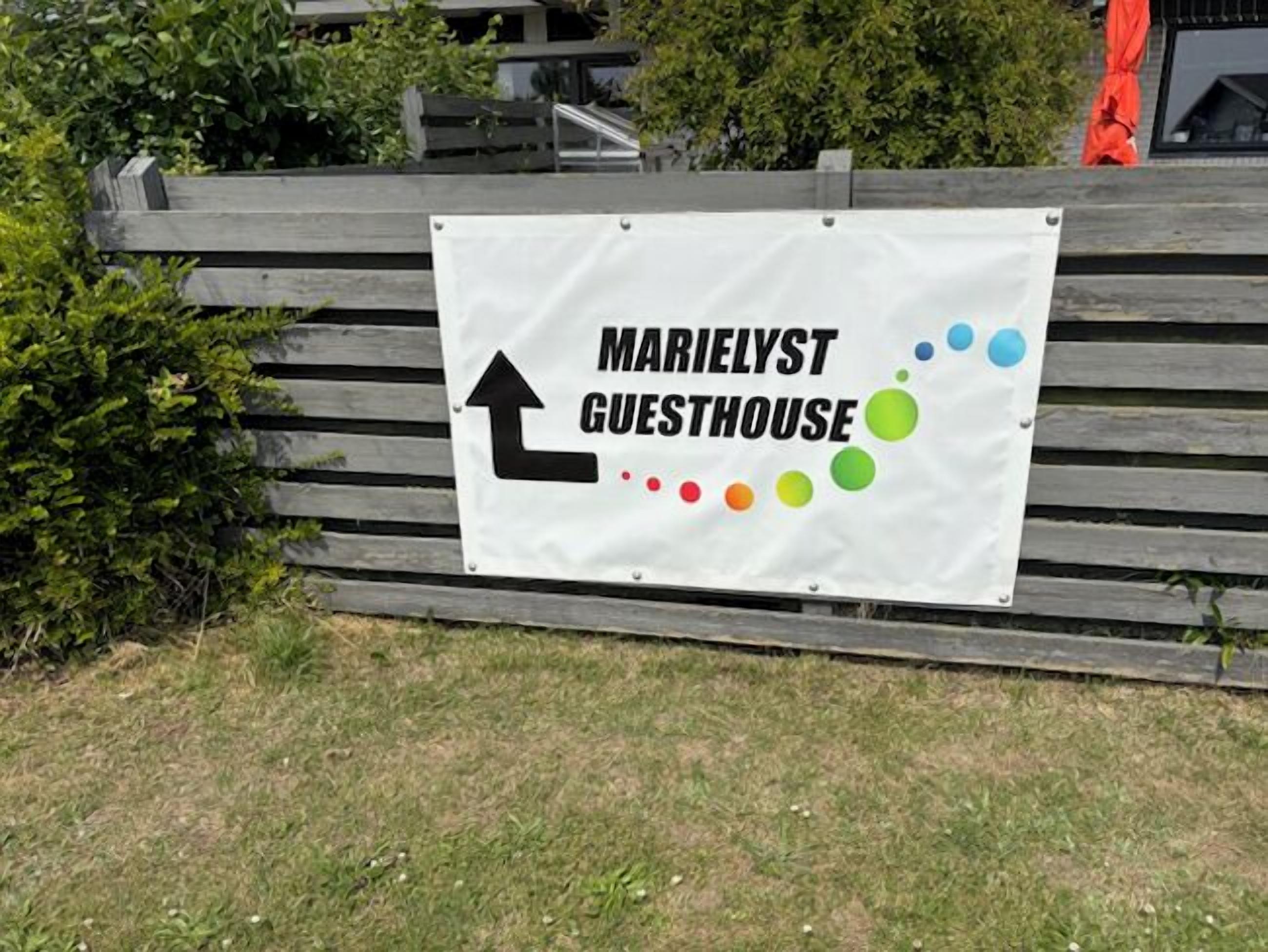 A sign for Marielyst Guesthouse with directional arrows and a colorful dot pattern.