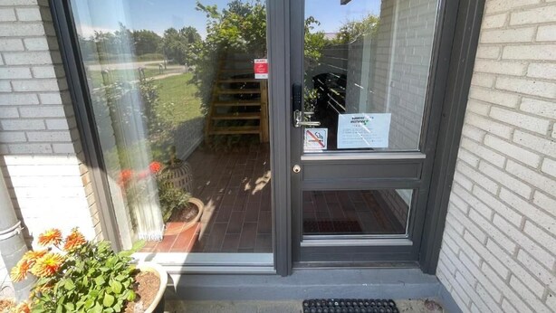 Eine Glastür mit Metallgriff, einem kleinen Schild und einem Blumentopf auf der linken Seite.