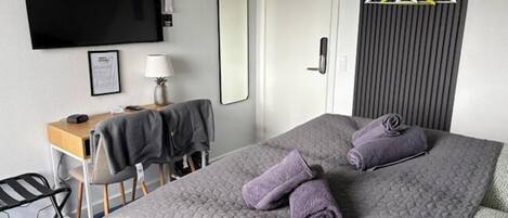 Una camera d'hotel con un letto, una scrivania, una sedia, una televisione, uno specchio e un appendiabiti.