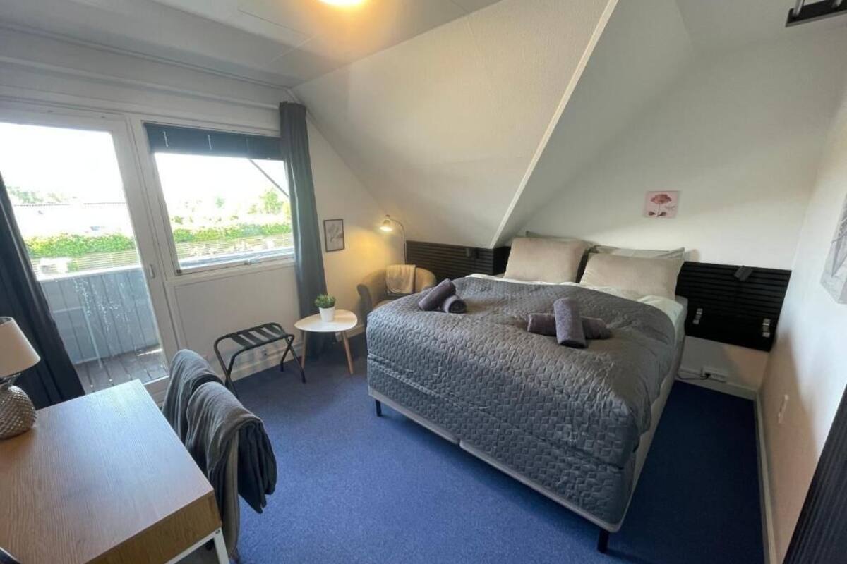 A bedroom with a bed, a desk, a chair, a small table, and a window.