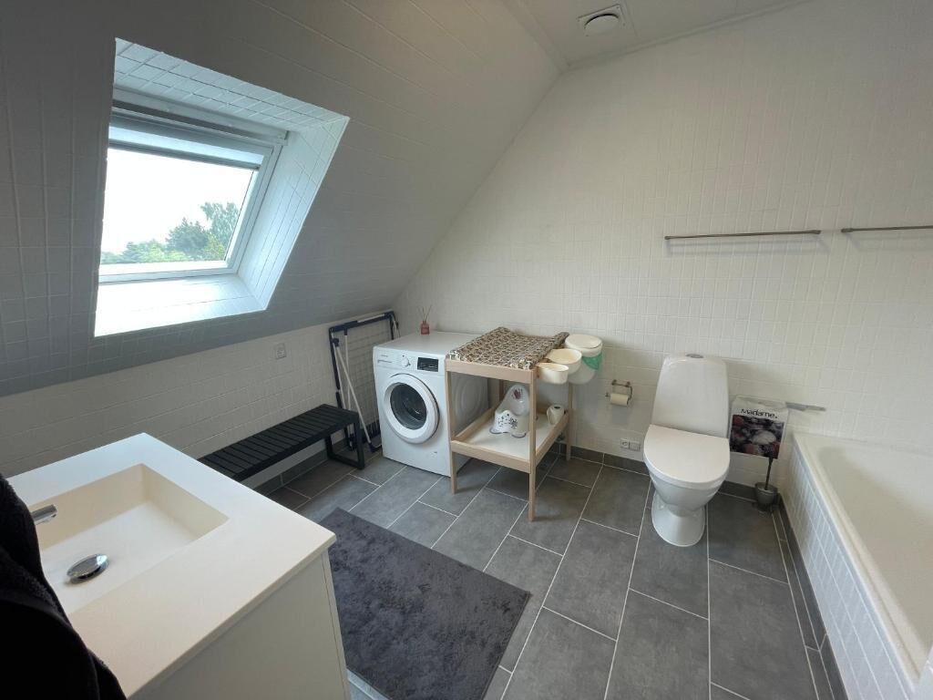 A compact, modern bathroom with a skylight, a washing machine, and a toilet.