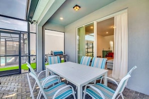 An outdoor patio with a white table and striped chairs, a grill, and a view of a pool.