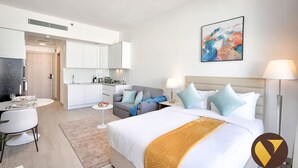 A modern hotel room with a large bed, a dining area, a kitchenette, and a bathroom.