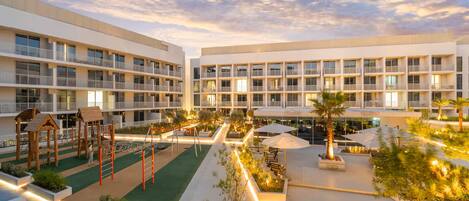 A multi-story hotel with balconies, a children's play area, outdoor seating, and landscaped gardens.