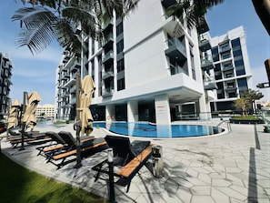 Un edificio moderno con zona de piscina, sillones de descanso y sombrillas.