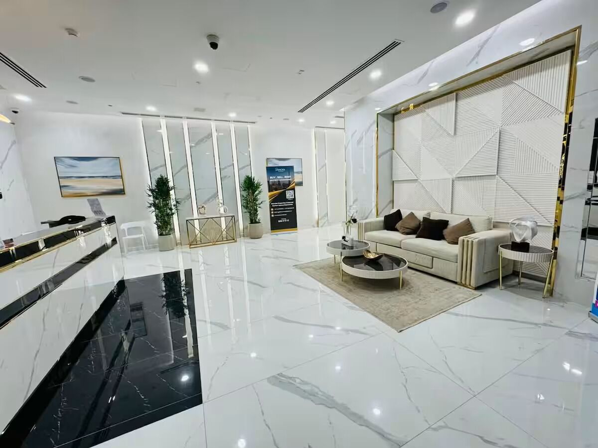 A modern hotel lobby with a marble floor, a reception desk, a seating area with a sofa and coffee table, and a decorative wall panel.