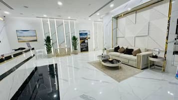 Un moderno vestíbulo de hotel con piso de mármol, un mostrador de recepción, una zona de estar con sofá y mesa de centro, y un panel decorativo en la pared.