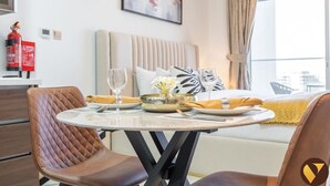 Een hotelkamer met een bed, een eettafel gedekt met borden, glazen en een bloevas. Op de muur staat een brandblusser en er is een raam met gordijnen.