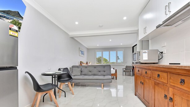 A modern kitchen with a built-in oven, a dining area with a table and chairs, and a grey sofa in the living room. - Coastal Bliss Studio at Shoal Bay (Shoal Bay)