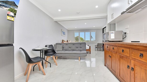 A modern kitchen with a dining area, a grey sofa, and a TV on the counter.