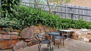 A patio area with a stone wall, two metal chairs, and a small table. - Coastal Bliss Studio at Shoal Bay (Shoal Bay)