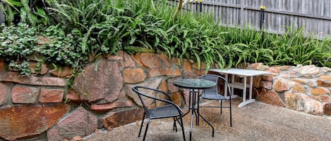 Een terras met een stenen muur, twee metalen stoelen en een kleine tafel.