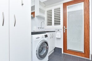 Een moderne wasruimte met een Bosch wasmachine, een houten deur en witte kastjes.