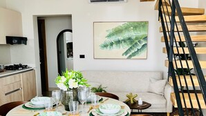 Un comedor con una mesa redonda dispuesta para cuatro personas, rodeada de sillas de madera. Se observa una escalera con escalones de madera y barandilla negra a la derecha.