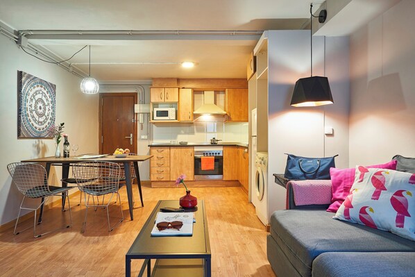 Un espace de vie compact comprenant un coin repas, une kitchenette et un canapé agrémenté de coussins décoratifs.