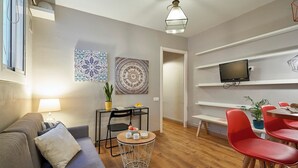 Een moderne woonkamer met een bank, een eettafel met stoelen, een aan de muur bevestigde televisie en kunstwerken aan de wanden.