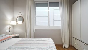 Een slaapkamer met een bed, een nachtkastje met een lamp, een spiegel, een raam met gordijnen en een kledingkast.