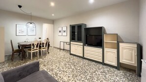 A modern living room with a dining area, featuring a TV, cabinets, and artwork on the walls.