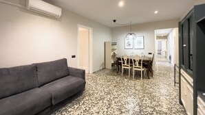 A living room with a grey sofa, a dining area with a table and chairs, and a hallway leading to other rooms.