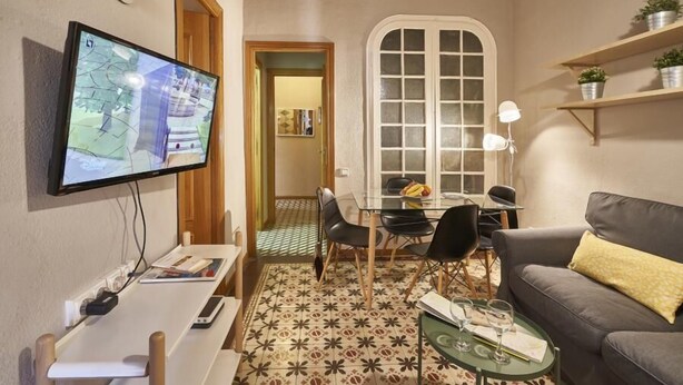 A cozy living room with a flat-screen TV, a dining area with a table and chairs, and a sofa.