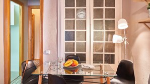 A dining area with a glass table, chairs, a fruit bowl, and a white lamp.