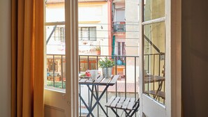 A balcony with a table, a potted plant, and a window overlooking a building with balconies.