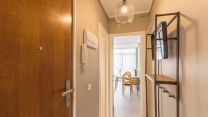 A hallway with a wooden door, a white wall, a ceiling light fixture, and a chair in the background. - Valles Atico · One bedroom apartment with terrace (Barcelona)