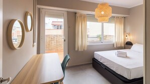 A hotel room with a bed, a desk, a chair, a window with curtains, and a hanging light fixture. - Valles Atico · One bedroom apartment with terrace (Barcelona)