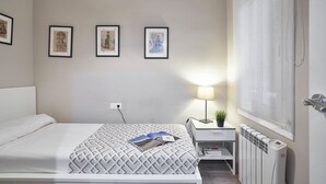 A neatly arranged bedroom with a bed, bedside table with a lamp, framed pictures on the wall, and a radiator.