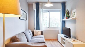 A modern living room with a sofa, a TV on a stand, a lamp, and a window with curtains.