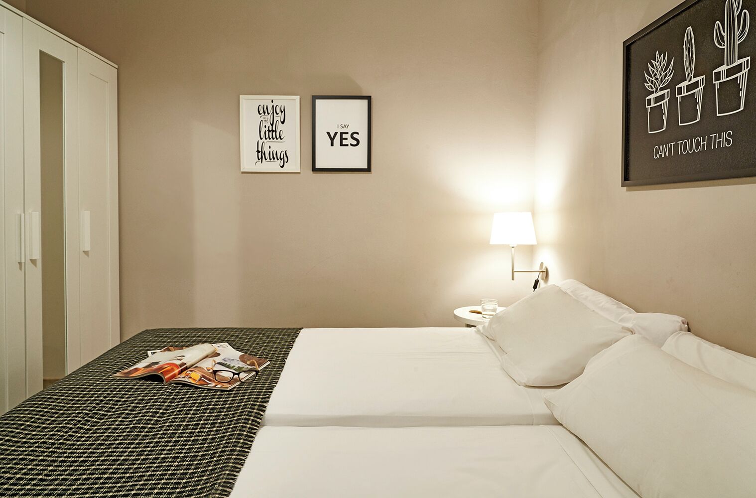 Een hotelkamer met een bed, een nachtkastje, een lamp en twee ingelijste motiverende citaten aan de muur.