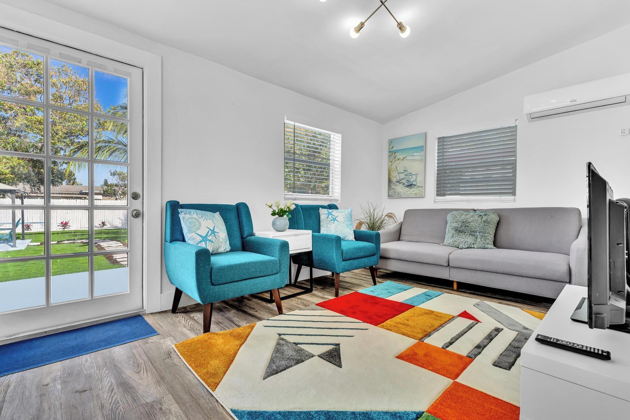 A modern living room with a grey sofa, teal armchairs, and a colorful rug.