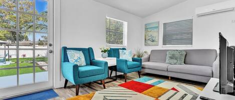 A modern living room with a grey sofa, teal armchairs, and a colorful rug.