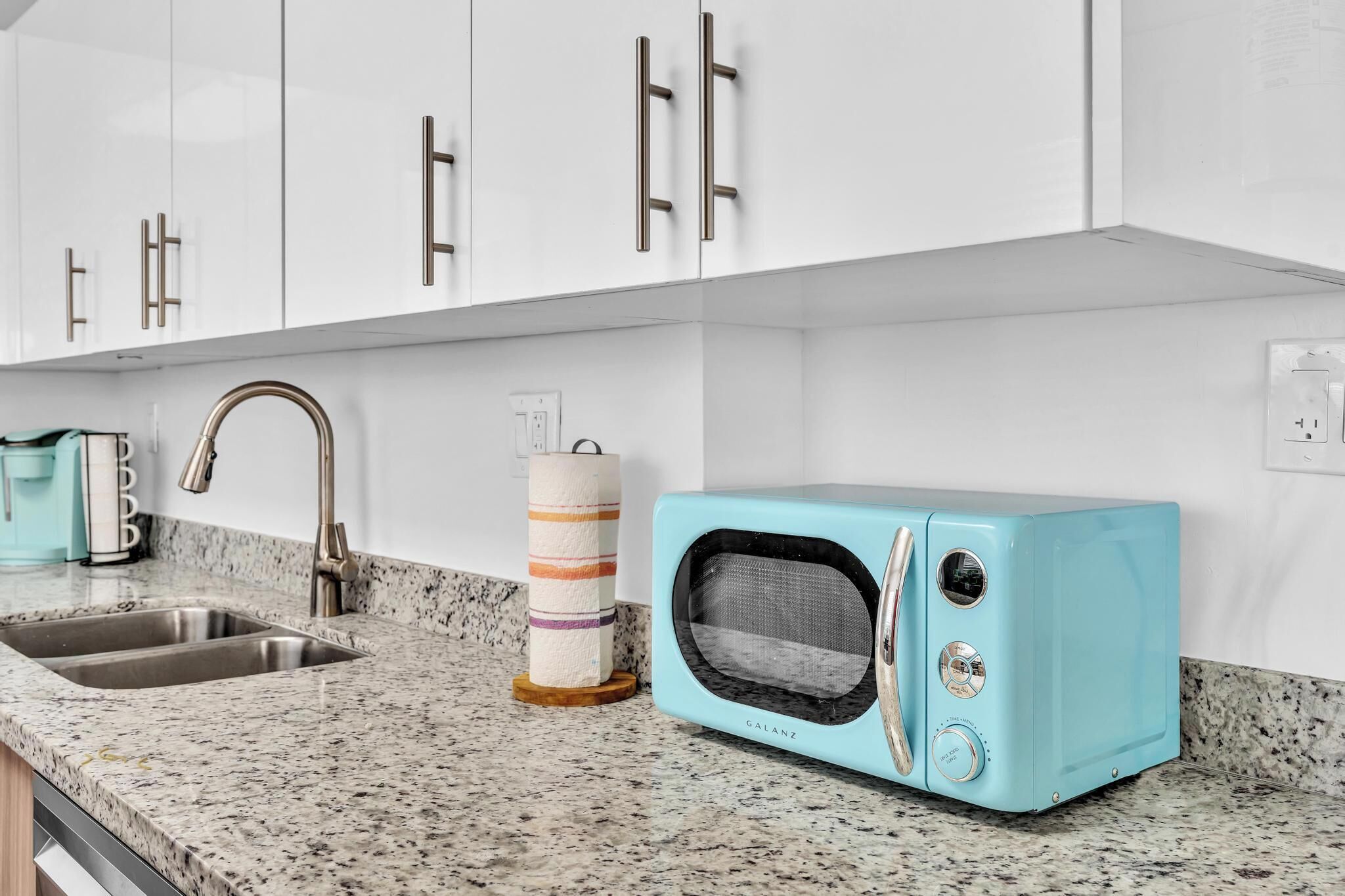 Eine Küche mit weißen Schränken, einer Granitabdeckung, einer Spüle, einem Toaster und Küchenpapier.