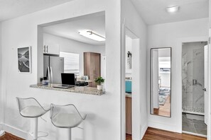 A modern kitchen with a built-in island, bar stools, and a large mirror. - Dreamy Hollywood Beach Escape | Fire Pit (Dania Beach)