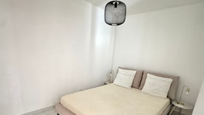 A bedroom with a bed, a nightstand, a small table, and a hanging light fixture. - Welcome to MBA HOUSE - Relaxation & Comfort in Guadeloupe! (Pointe-à-Pitre)